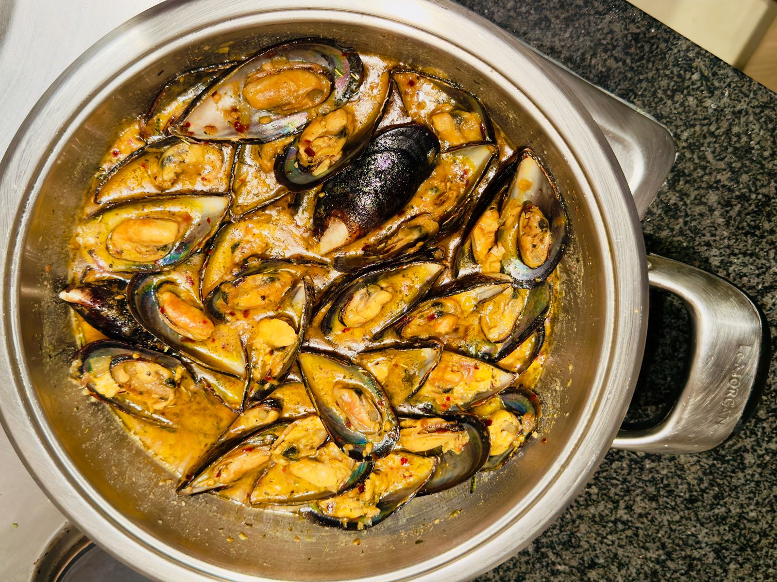 Easy creamy mussels recipe cooking in a pot with onions, fish spice, turmeric, and fresh cream.